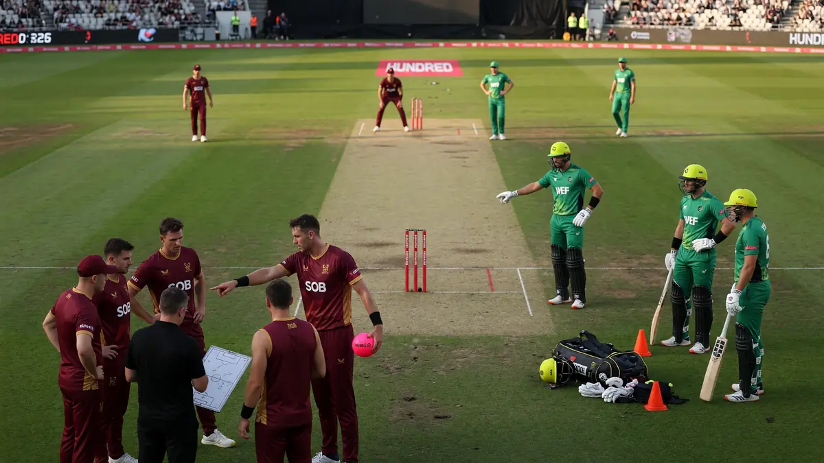 Maroon Southern Brave and green Welsh Fire players talking near the pitch with a pink ball and field map during a stoppage
